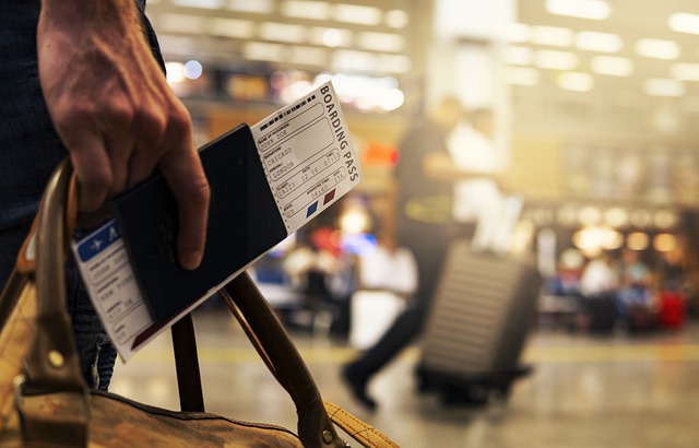Mano di uomo in un aeroporto che tiene in mano un borsone, il passaporto e il biglietto aereo per andare in vacanza.
